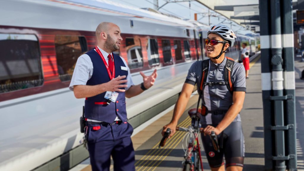 A railway passenger with a bicycle talking to a railway member of staff.