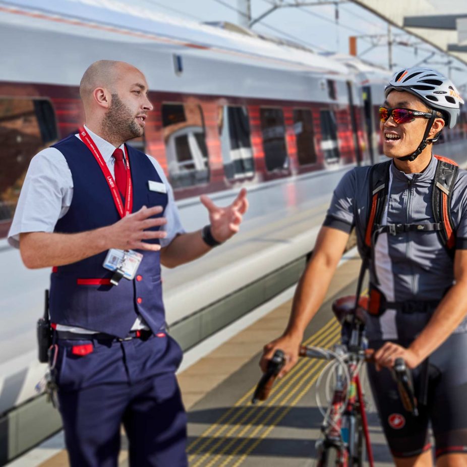 A railway passenger with a bicycle talking to a railway member of staff.